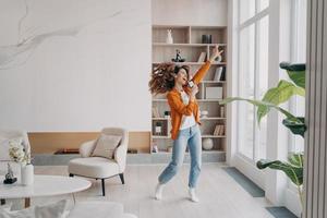 Energetic woman holding smartphone, having fun, dances to music rejoicing with good news at home