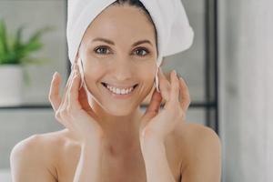Happy woman cleansing face, removing makeup by cotton pads after shower. Beauty treatment, skincare photo