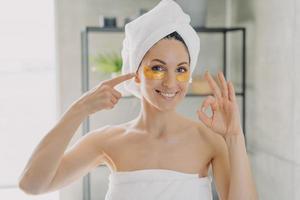 Pretty woman advertising anti wrinkles anti age eye patches showing ok gesture in bathroom. Skincare photo