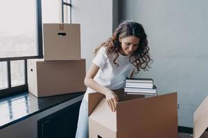 Happy woman packing carton box with things, relocating in new home. Moving, real estate rental photo