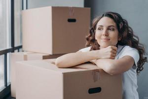 Happy female with cardboard boxes resting during packing things, dreaming about new home. Moving day photo