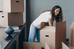 Hispanic woman unpack boxes with delivered things during relocation at new home. Moving, delivery photo