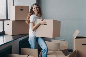 Excited girl carrying carton box with things for relocation to new home apartment. Mortgage, moving photo