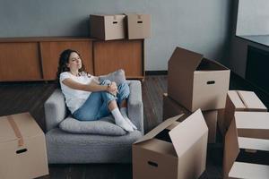 Relaxed woman rests in armchair during packing things for moving at new home. Mortgage advertising photo