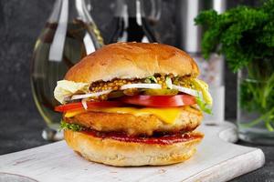 Tasty chicken burger with lettuce, cheese, tomato and pickle. Fast food sandwich with chicken cutlet photo