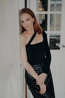 mujer adulta joven en negro. modelo con falda de cuero y manga larga slim fit delante de la puerta. foto