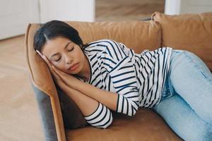 Young exhausted hispanic woman is sleeping. Overworked lady fell asleep in living room. photo