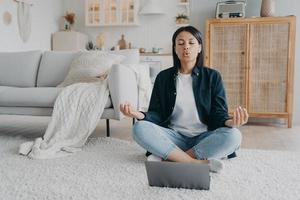 la mujer practica yoga en la computadora portátil, respira profundamente sentada en el suelo en casa. alivio del estrés, meditación