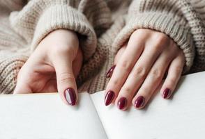 manos de una mujer joven con manicura roja oscura en las uñas foto