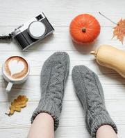 Legs of a girl in knitted socks on a wooden background next to pumpkins and autumn leaves photo