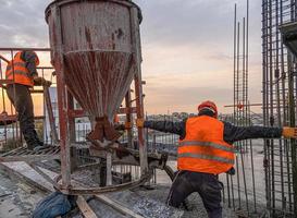 The workers on a building infrastructure roof with machinery and tools. Pouring concrete into a mold photo