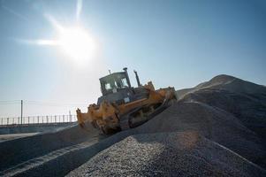 una excavadora pesada en una montaña de carga de grava contra el cielo soleado foto