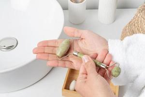 female hand holding jade massage face roller in bathroom photo