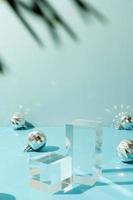 A minimalistic scene of glass podium with christmas decorative balls and pine tree on a light blue background photo