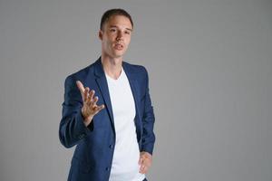 A male businessman in a blue jacket on a gray background gestures to the side, copy space photo