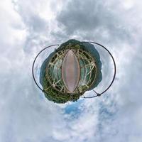 tiny planet in blue overcast sky with beautiful clouds with transformation of spherical panorama 360 degrees. Spherical abstract aerial view. Curvature of space. photo