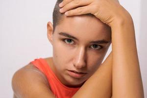 Caucasian girl with short hair, almost bald, holds her hands behind her head photo