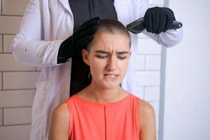 Young woman is forcibly shaving her head with an electric razor, holding photo