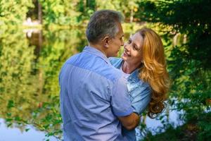 Happy mature couple embracing and embracing in thickets headland near lake are photo