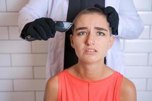 Young woman is forcibly shaving her head with an electric razor, holding photo