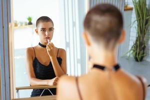 a girl with short hair paints her lips, looks in the mirror in black clothes photo