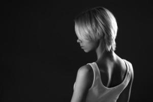 young sad woman looks away, a dark black and white photo. Stands sideways . photo