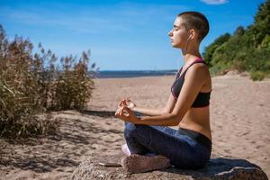 mujer elegante haciendo yoga asana en la playa en auriculares medita en la orilla del mar foto