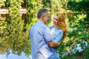 feliz pareja madura abrazándose y abrazándose en matorrales cerca del lago son foto