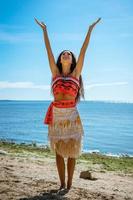 woman stands on the beach against the sea and raises her hands in the air photo