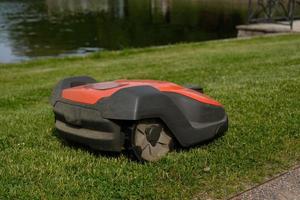 Robotic Lawn Mower on green grass background.Automatic robot lawnmower in modern garden.Green grass trimming with lawn mower. Close-up view of the lawn mower dirty blade after mowing the lawn. photo