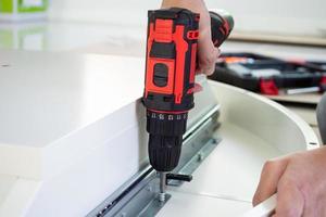 man assembling white table furniture at home using cordless screwdriver photo