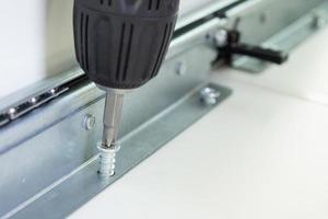 man assembling white table furniture at home using cordless screwdriver photo