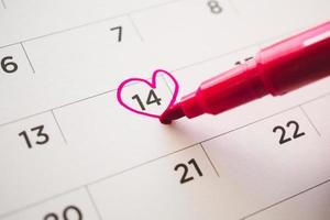 Female Hand with pen mark heart shape on calendar date at 14th valentine day photo