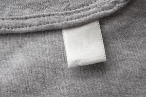 Blank white laundry care clothes label on gray fabric texture background photo