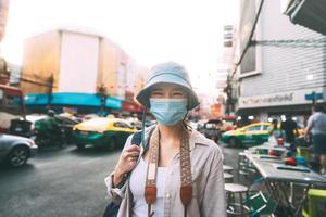 Walking young adult asian woman traveller wear face mask for covid-19 traveling in local city on summer day. photo