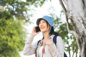 Young adult asian woman traveller wear blue hat and backpack using mobile phone internet for calling on travel. photo