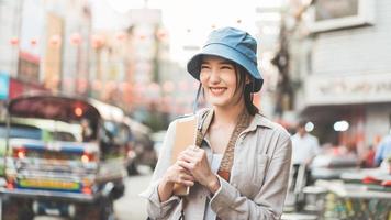 Solo young adult asian woman traveller wear blue hat and backpack travel with modern technology at outdoor on day. photo