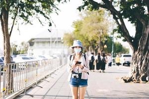 una joven viajera asiática adulta que camina usa una máscara facial para covid-19 que viaja en la ciudad local el día de verano.