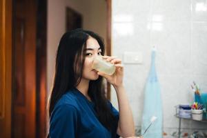 Young adult asian woman brushing teeth in bathroom photo