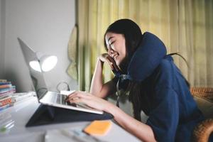 Young adult freelancer asian woman using laptop wear neck pillow in workplace space on night shift at home. photo