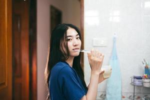 Young adult asian woman brushing teeth in bathroom photo