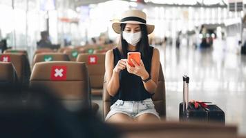 una joven turista adulta usa una máscara para el brote de virus en la terminal del aeropuerto con una silla de distanciamiento social.