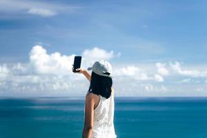 Rear view of adult asian woman relax in nature using smartphone take a selfie photo