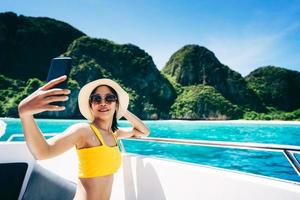 Travel influencer adult woman wear bikini using mobile phone for live video on the boat with summer tropical background. photo