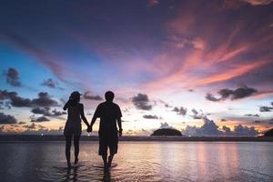 Rear view of adult tourist asian love couple holding hand on the beach with sunset sky background photo