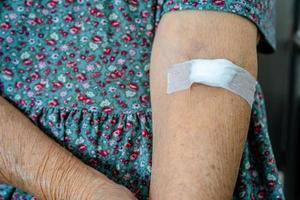 Asian senior or elderly old lady woman patient show cotton wool stop bleeding, after blood drawing testing for annually physical health check up to check cholesterol, blood pressure, and sugar level. photo