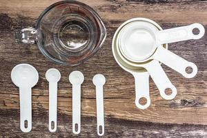 juego de tazas de medición blancas, cucharas de medición y uso de vidrio de medición en la cocina sobre una mesa de madera en la vista superior foto