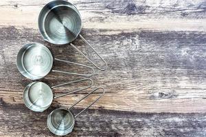 Set of measuring cups made from stainless with a handle on wooden tabletop in top view photo