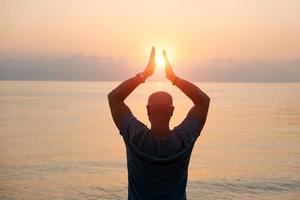 Silhouette man with his hands raised at sunset on beach arms out to sides photo