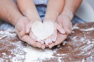 vista superior de la mano del padre y del niño, corte las galletas en forma de corazón de la masa foto